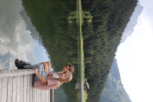 Two children are sitting on a wooden dock, gazing out over a calm lake